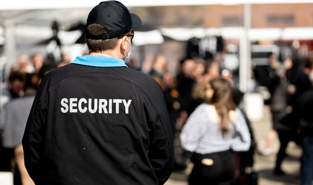 Agile Security - Security Professional watching people at an event, shown from behind with security vest showing
